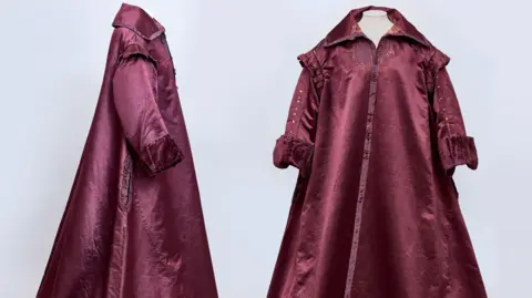 A side and front view of a 1600s era gown. It is a burgundy colour and has a collar.