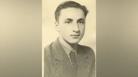Family Handout Wilhelm Reuhl sits for an official photo. He is looking away from the camera. He has dark hair and is wearing a suit jacket and tie. It's a black and white picture. 