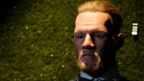 National Wax Museum Plus Patung lilin Conor McGregor dalam setelan jas berdiri di depan latar belakang hijau.