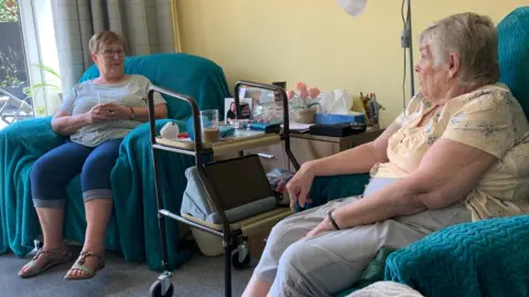 Barbara Skedd and Catherine Lockwood, sitting on a sofa talking at Skedd's home in Ibstock, Leicestershire.