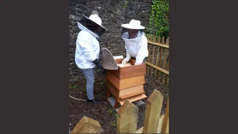 Rochester Cathedral Two beekeepers standing behind a wooden fence and arranging a newly-installed beehive at Rochester Cathedral gardens.