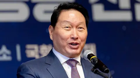 Getty Images Close-up photo of Chey Tae-won speaking on a microphone wearing a suit and tie against a blurred blue and white background