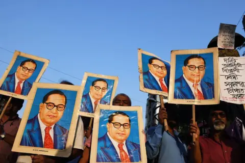 AFP via Getty Images Indian activists holds portraits of 20th century Indian social reformer B. R. Ambedkar while shouting slogans during a protest against a Supreme Court order that allegedly diluted the Scheduled Castes and Scheduled Tribes (Prevention of Atrocities) Act in Kolkata on April 4, 2018. Street battles and widespread protests by Indian 'low-caste' groups enraged by what they consider the undermining of a law protecting their safety left at least one dead, police said. Clashes with police, attacks on buses and government buildings, blocked trains and roads were reported across five Indian states. / AFP PHOTO / Dibyangshu SARKAR (Photo credit should read DIBYANGSHU SARKAR/AFP via Getty Images)
