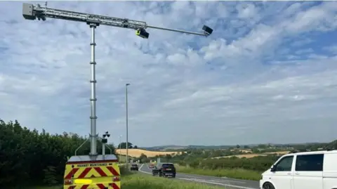 Vision Zero South West A vehicle by the side of the road which has red and yellow markings. There is a white van and other vehicles on the road. 