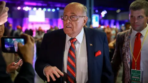 Getty Images Rudy Giuliani wears a blue suit and red tie with glasses