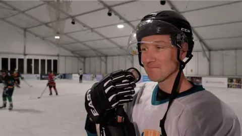 Gavin Glazier is in a white top. He is seen looking off camera. He is wearing a black helmet, a white shirt and black gloves.