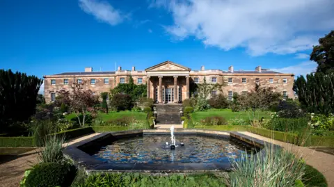 Getty Images Hillsborough Castle building, with a pond in front of it. There is a blue sky above. 