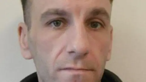 A mugshot of a man who looks at the camera unsmiling. 