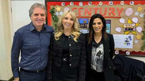 Steve Rotheram, in a blue shirt, Kate Peaston, in black dress and Priya Lakhani, in a black blazer smile in front of the camera in front of a display board with 'Century' spelled out on it