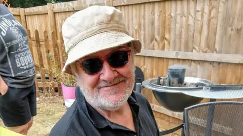 David Phillips David Phillips with short white beard wearing a beige sun hat and sunglasses at a barbeque