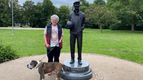 A woman with a boxer cross stands next to a statue to Jack Charlton 