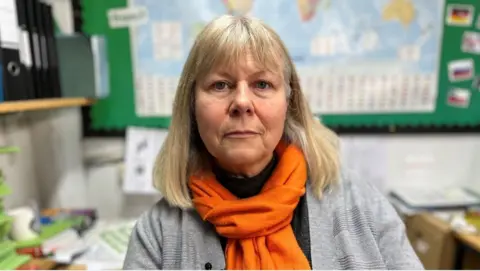 A woman sat in an office wearing a grey cardigan and an orange scarf.