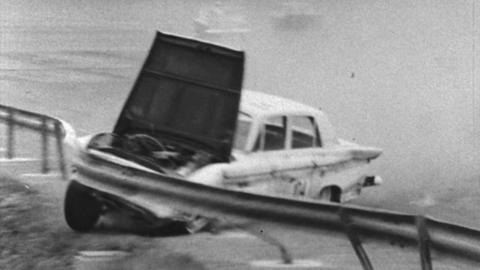 A black and white image of a car crashing into a motorway barrier, with the bonnet flying up.