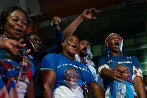 ERNEST ANKOMAH/GETTY IMAGES People dressed in blue sing, dance and wave their arms in the air.