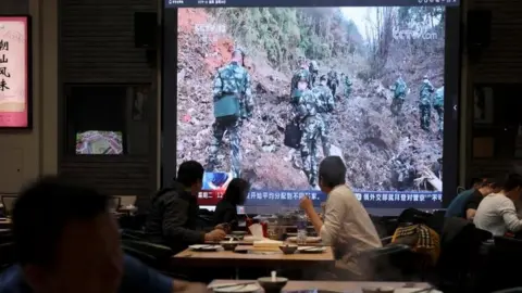 Reuters Diners in a restaurant watch a TV news broadcast showing soldiers working at the crash site of the flight in Wuzhou