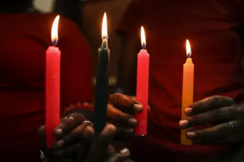 EPA Two pink candles, one green and one yellow are seen close up, held in the hands of two different people who are both wearing red tops in Nairobi, Kenya - Sunday 17 February 2019