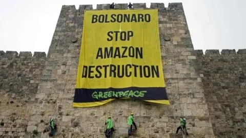 AFP Greenpeace activists hang a large banner on the ramparts of the Old City of Jerusalem with a message to the visiting Brazilian president, on April 1, 2019