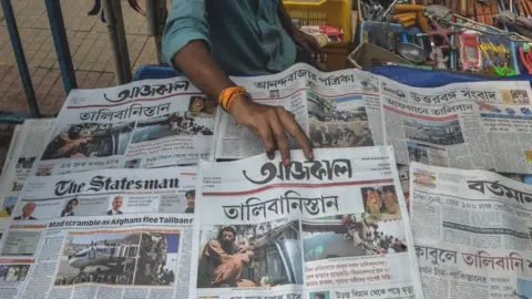 A newspaper vendor arranges newspapers displaying front page news about Afghanistan in Siliguri on 17 August, 2021