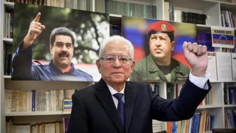 AFP Ambassador Jorge Valero poses between photographs of President Nicolas Maduro (L) and late President Hugo Chavez during a interview with AF