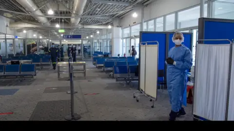 Getty Images Medical staff wait to conduct tests on passengers arriving at Eleftherios Venizelos International Airport in Athens