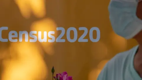 AFP via Getty Images A man wearing a facemask walks past a sign encouraging people to complete the 2020 US Census, in Los Angeles, California, August 10, 2020