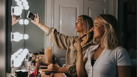 Getty Images Two women doing make-up with phone