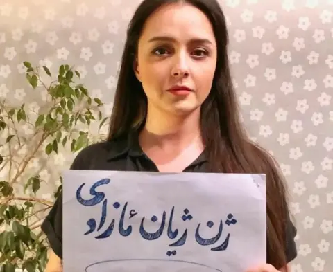 TARANEH ALIDOOSTI VIA INSTAGRAM Taraneh Alidoosti poses for a photograph without a headscarf and holding a sign bearing the protest slogan: "Woman, life, freedom"