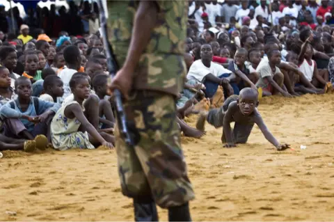 Jonathan Banks A boy from a crowd retrieves his ball from the shadow of armed security at the Liberia National Peace and Cultural Festival in Monrovia