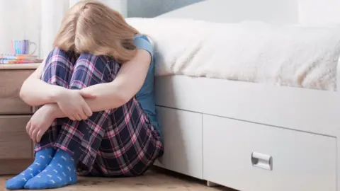 Getty Images Girl sitting with head on her knees on the floor