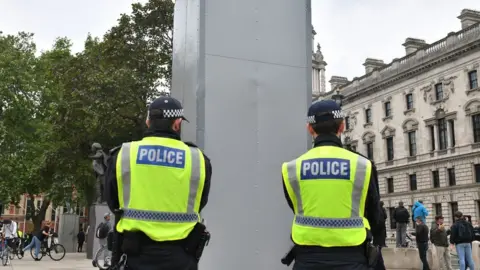 PA Media Police officers stand beside the now encased Churchill statue on Parliament Square