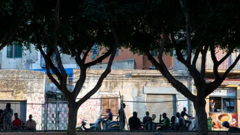Kate Stanworth Migrants sitting at outside tables in alermo's Ballarò neighbourhood - Sicily
