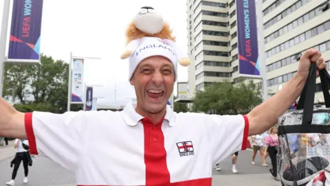 PA Media A male football fans holds his arms up as he stands on Wembley Way