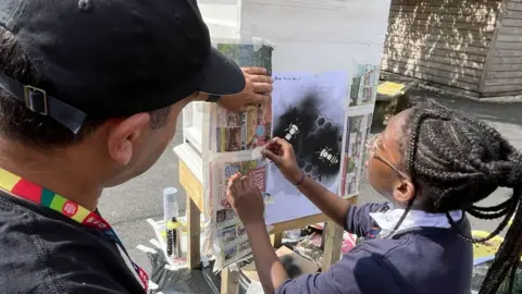 Martin Giles/BBC Street artist Emo helping a school pupil at a spray painting workshop