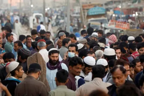 Reuters A man wearing a protective mask walks through a crowd of people along a makeshift market as the outbreak of the coronavirus disease (COVID-19) continues, in Karachi, Pakistan January 17, 2021.