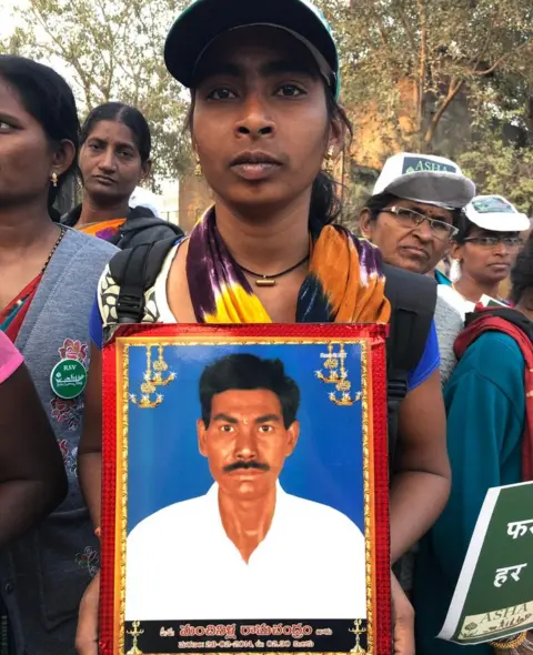 The daughter of a farmer who killed himself is seen in the protest, carrying a photograph of her father.