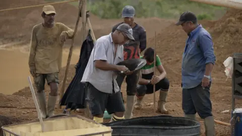 Bernard Christopher Alphonso looks at specks of gold at his mine