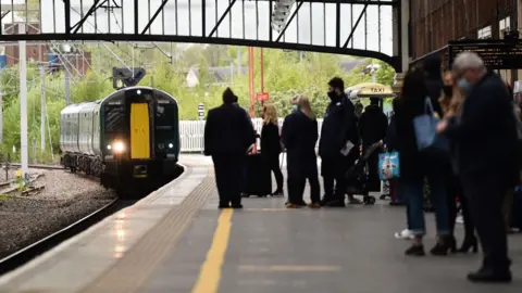 Getty Images People waiting at a train station as a train approaches them