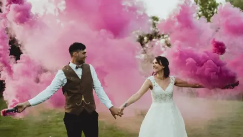 Georgia Rachel Marries couple pose for wedding photo with pink smoke bombs in the background