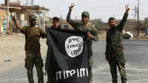 AFP Iraqi members of the Hashed al-Shaabi (Popular Mobilisation units) carry an upsidedown Islamic State (IS) group flag in the city of al-Qaim, in Iraq"s western Anbar province near the Syrian border as they fight against remnant pockets of Islamic State group jihadists on November 3, 2017.