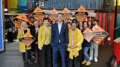 BBC Mr Blackie stands in front of a small crowd of supporters holding orange party signs