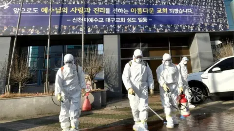 AFP/Getty Images Workers spray disinfectant in front of the Daegu branch of the Shincheonji Church of Jesus, the Temple of the Tabernacle of the Testimony. Photo: 19 February 2020