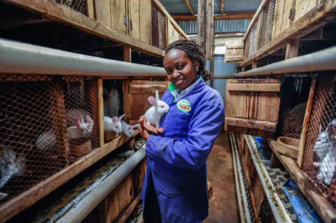 Anadolu Agency A woman stands next to rabbit hutches and holds a white rabbit.