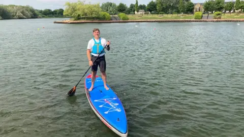 Justin Dealey/BBC Joe Cartwright on a paddleboard on Willen Lake in Milton Keynes