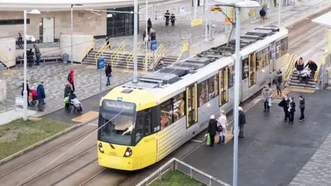 Tfgm tram at station surrounded by commuters