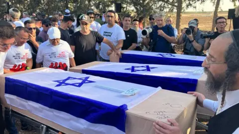 Laurie Margolis Three coffins draped in Israel flags, surrounded by mourners and journalists