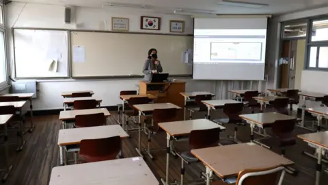 Getty Images A teacher wears a mask as she gives a lesson on the first day of online class in an empty classroom