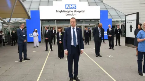 PA Media Health Secretary Matt Hancock and NHS staff stand on marks on the ground, put in place to ensure social distancing guidelines are adhered to, at the opening of the NHS Nightingale Hospital at the ExCel centre in London