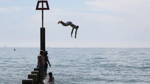 PA/Andrew Matthews A man jumps off a groyne into the sea as they enjoy the hot weather at Bournemouth beach in Dorset