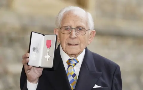Andrew Matthews/PA Media Harry Olmer holding up his MBE