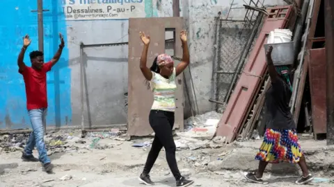 Reuters Residents raise their arms as they flee their homes due to ongoing battles between rival gangs. Port-au-Prince, Haiti, 2 May 2022.